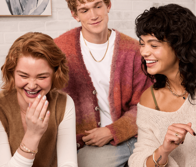 Group of three friends laughing. Each is wearing various fashion jewelry, including chains, bracelets and rings.