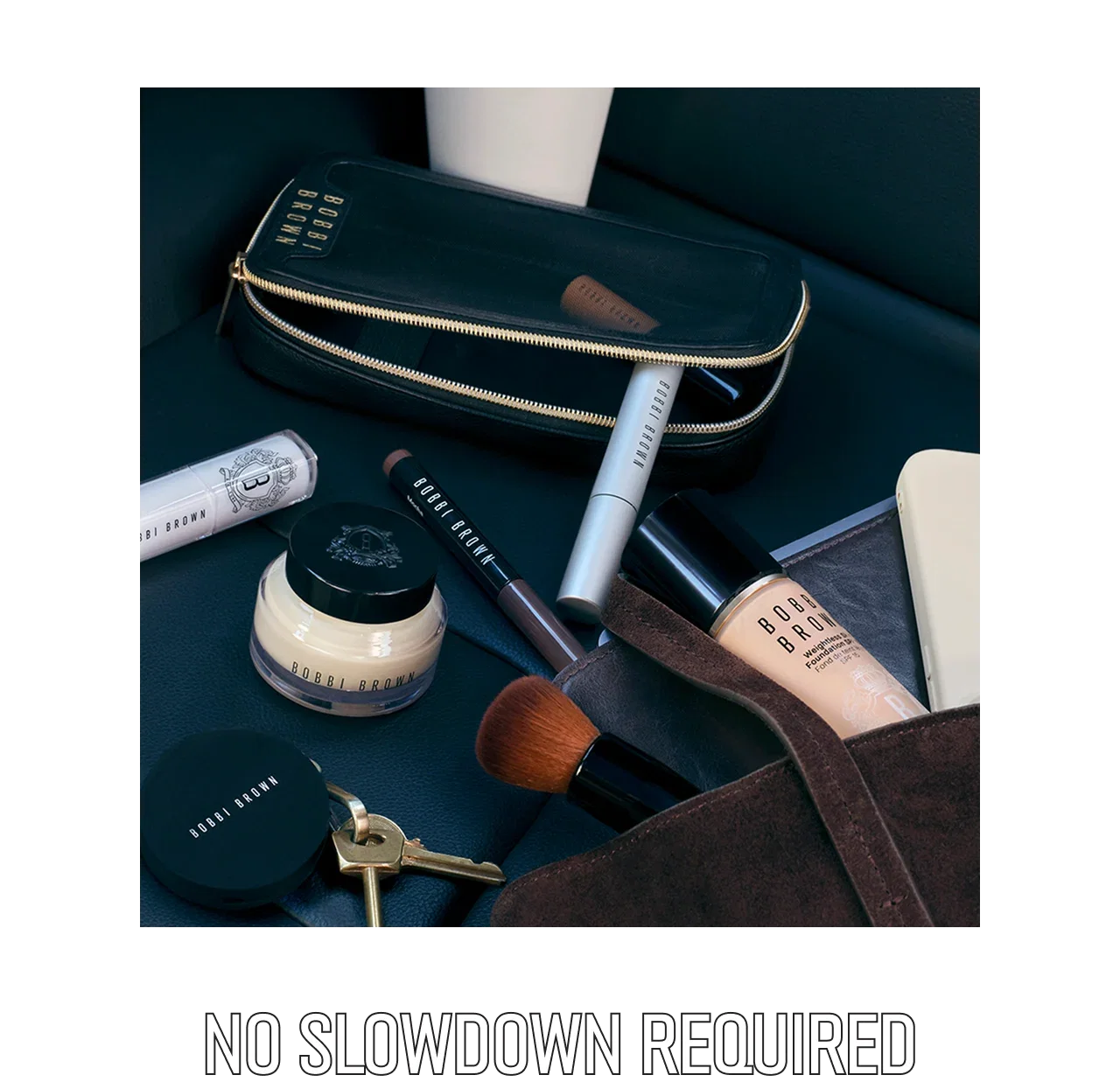 A collection of Bobbi Brown makeup items arranged on a dark leather surface with text below reading, 'No Slowdown Required'.