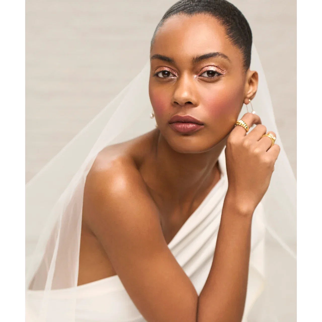 Woman wearing a wedding dress and veil with glowy makeup.