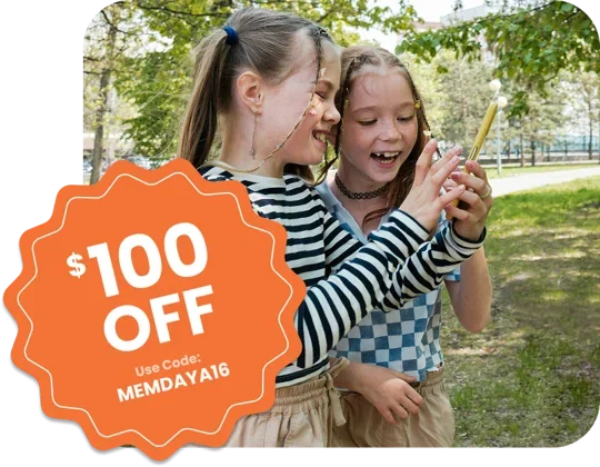 A photo is shown of two girls in a park looking at a smartphone. A badge on the image says $100 OFF. Use Code: MEMDAYA16