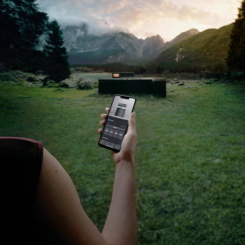 Eine Hand, die ein Smartphone hält, mit dem eine Miele Outdoor-Küche gesteuert wird.
