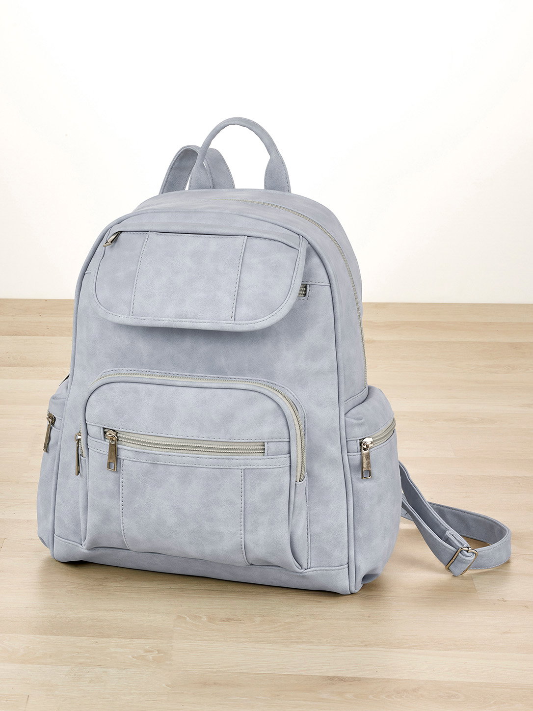 Ein Rucksack in bleu mit mehreren Reißverschlusstaschen und verstellbaren Schultergurten, steht auf einem Holzboden.