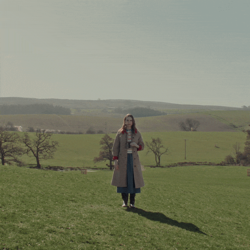 A woman in a field with binoculars spots a cow