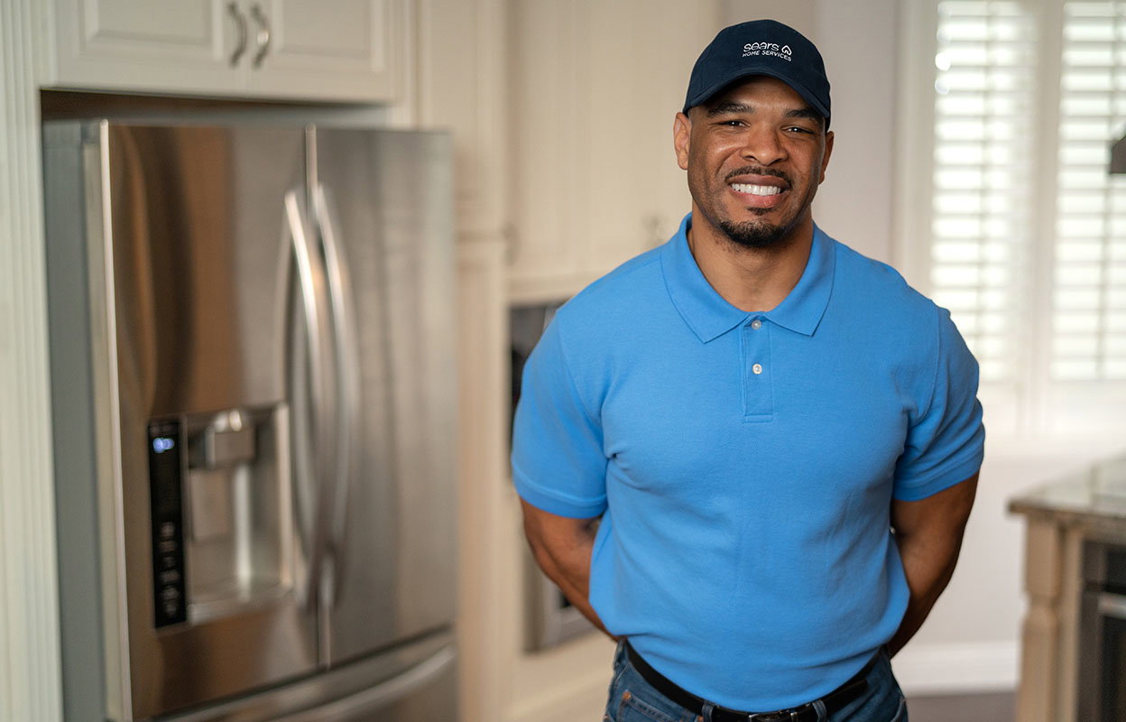 A smiling Sears Home Services technician in front of a fridge