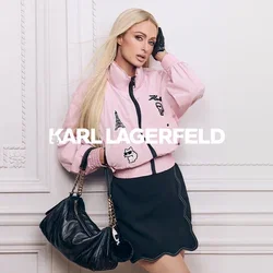 Vrouw met lang blond haar draagt een roze jas met patches, een zwarte rok, zwarte handschoen, en houdt een zwarte handtas met een gouden kettingriem vast.