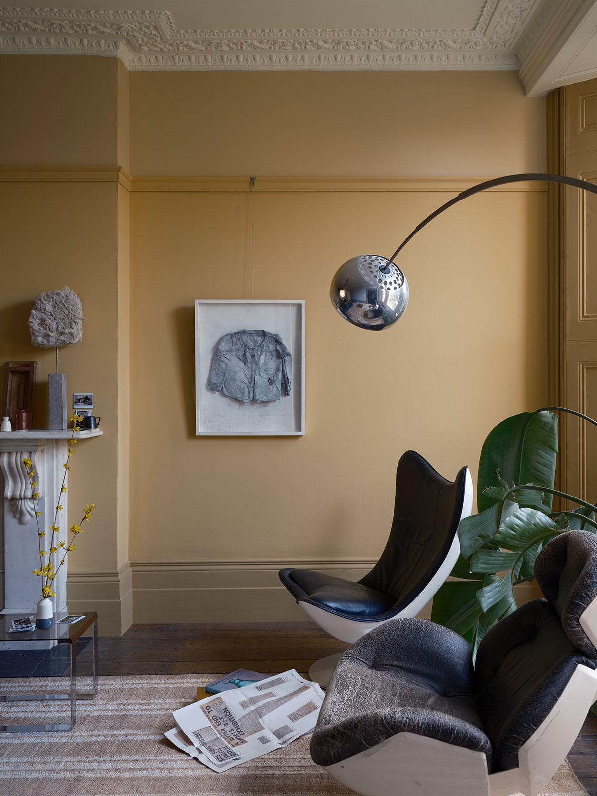 A modern living space layered in soft yellow hues, enhanced by daylight flooding through floor-to-ceiling windows. Sculptural chairs, a chrome lamp and simple artwork give the room a relaxed yet stylish look.
