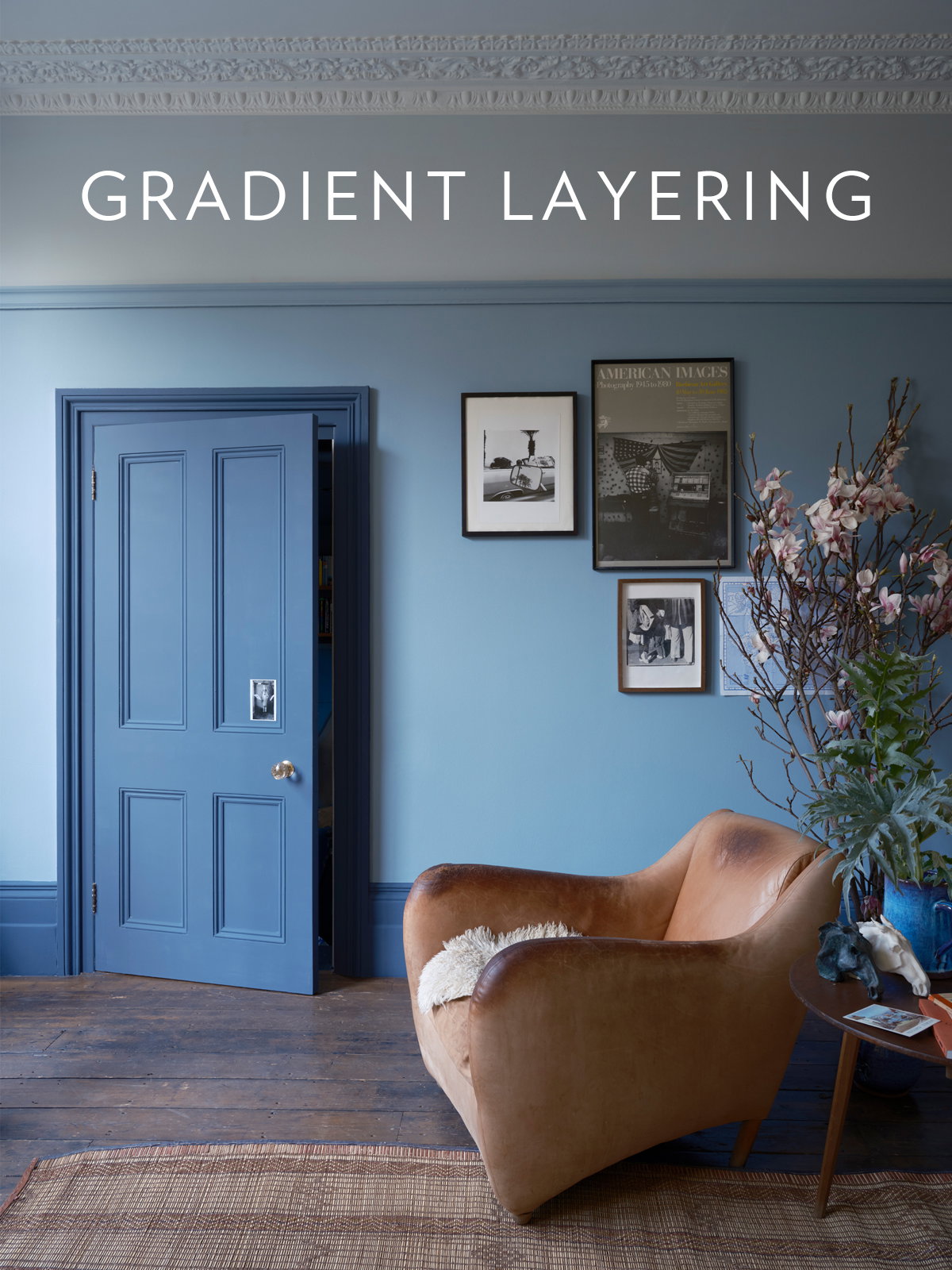 Layers of cool blues work together in this living room, with mid-blue walls, pale blue ceiling and dark blue door and skirting. A brown leather armchair, fresh flowers and framed artwork add character to this serene, thoughtfully composed space.
