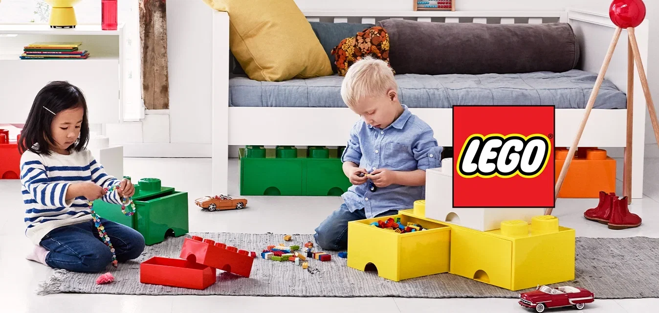 Zwei Kinder sitzen auf dem Boden und spielen mit großen, bunten Bauklötzen in einem hellen, modernen Spielzimmer.