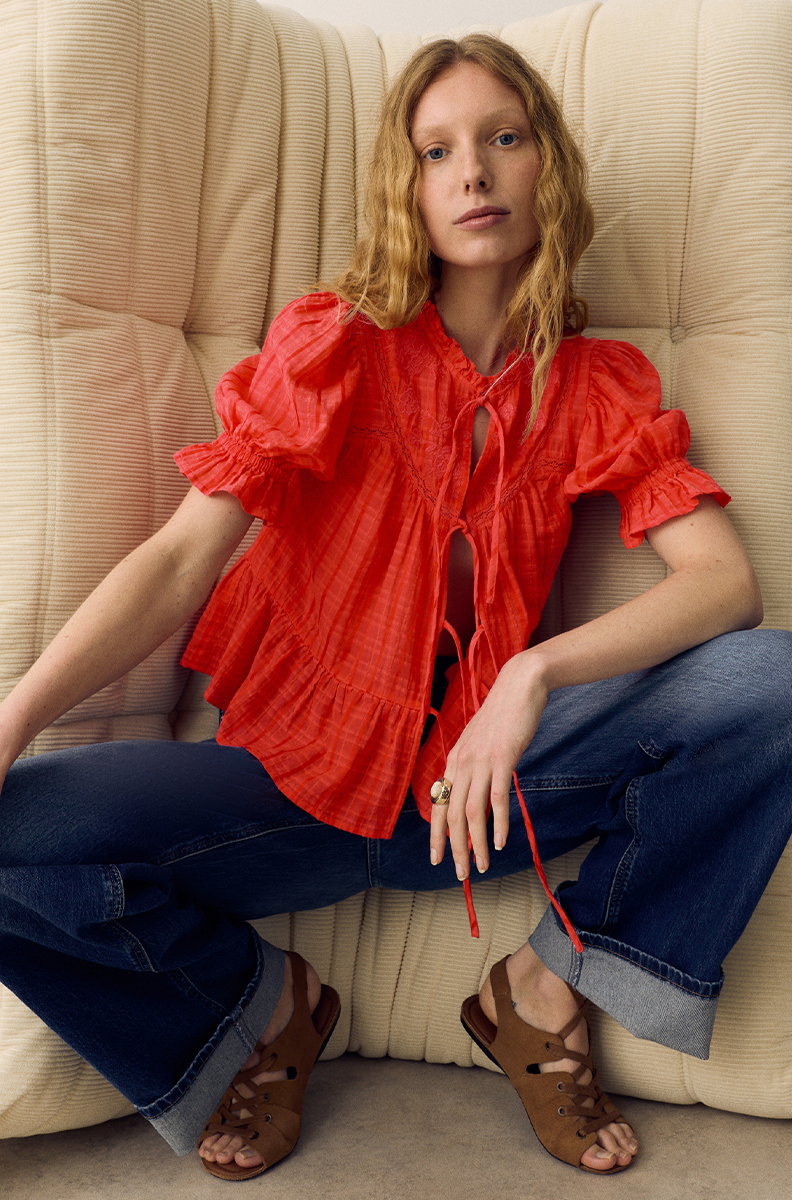 Woman crouching wearing Per Una Cotton Rich Embroidered Yoke Tie Neck Blouse in Bright Orange