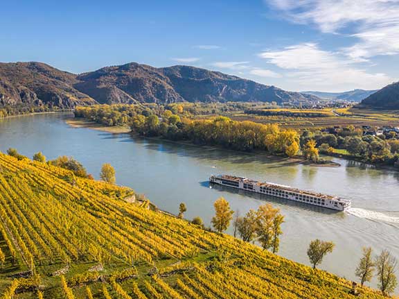 Flusskreuzfahrtschiff fährt entlang von Weinbergen an einem sonnigen Tag.