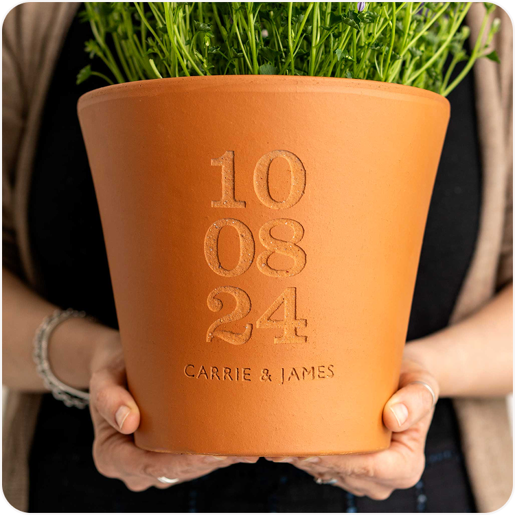 A pair of hands holding an engraved terracotta pot personalised with a special date