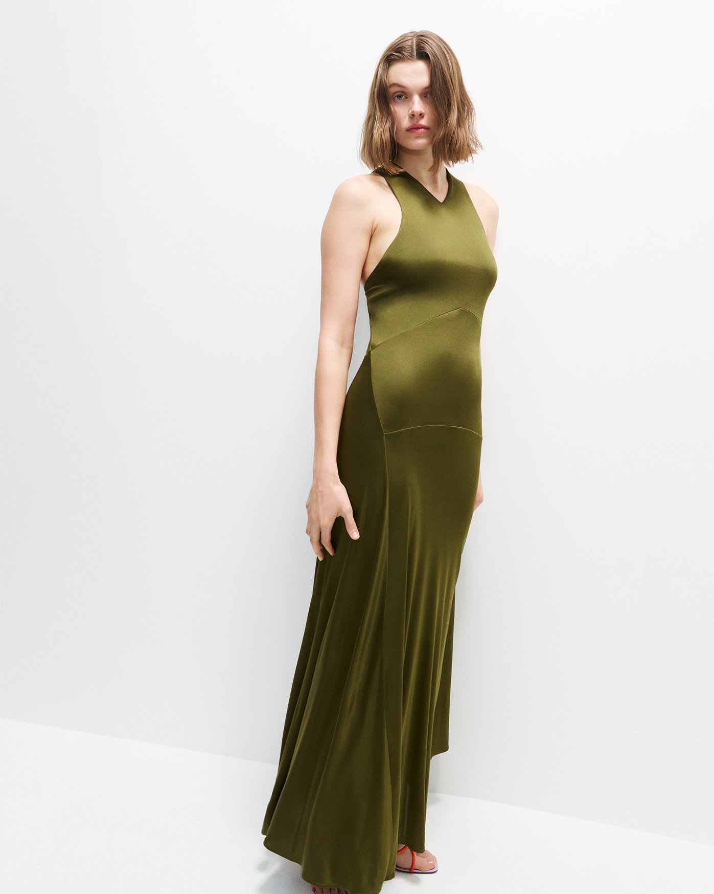 Image of model standing against a white wall and floor, wearing the Naia Dress in Viscose Satin Jersey in Moss with the Twist Slant Sandals in Marzipan / Lilac / Flame Combo 