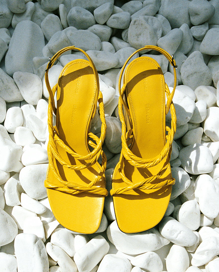 Still Life image of Twist Slant Sandals in Sun placed on a bed of white rocks
