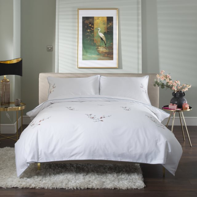 Elegant bedroom with a plush bed, floral bedding, side tables, and a painting of a heron above the headboard. Cozy and stylish decor.