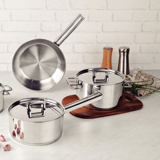 Stainless steel cookware set on a kitchen counter with some garlic and herbs.
