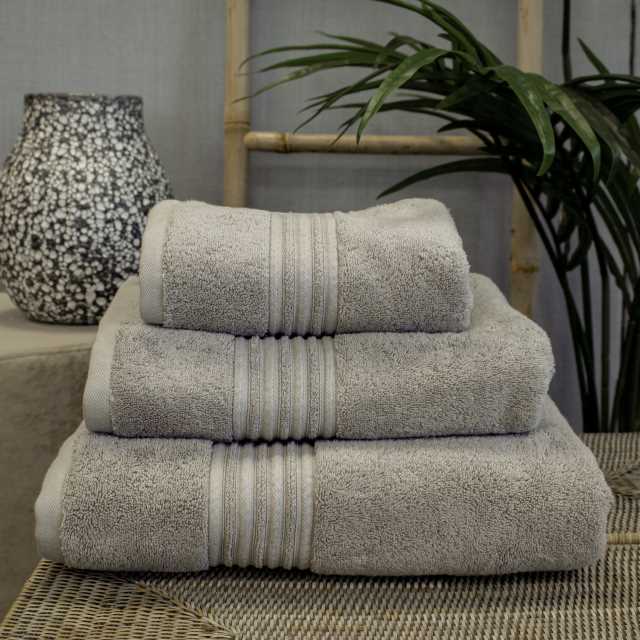 A stack of folded gray towels on a woven surface, with a textured vase and green plant in the background.