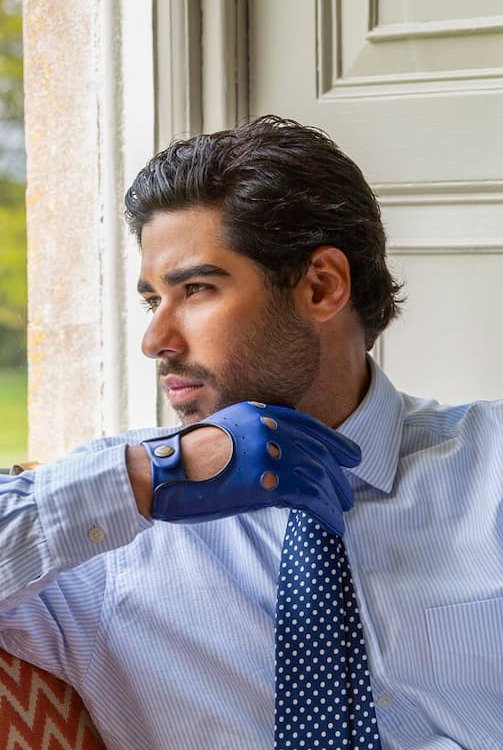 Man wearing leather driving gloves in royal blue sitting on a chair in the lounge