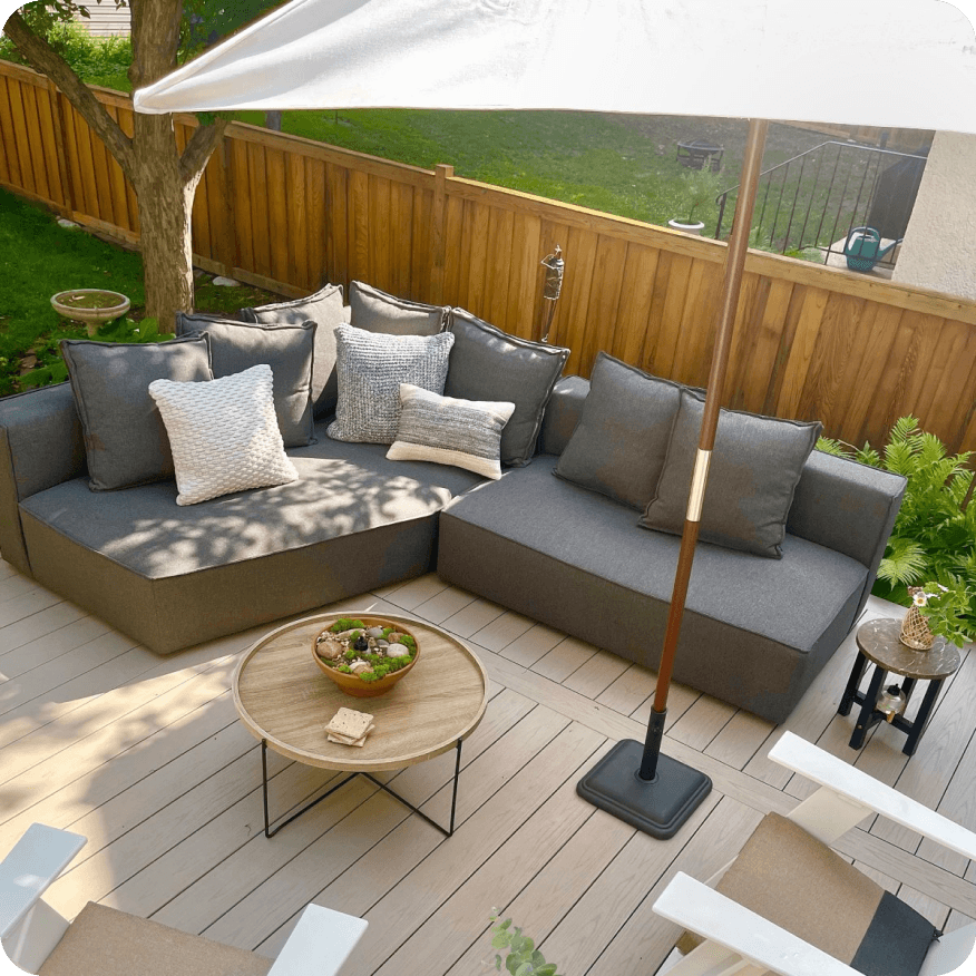 Oasis sofa with chaise in grey upholstery, styled with pillows around a round wood table on a deck.
