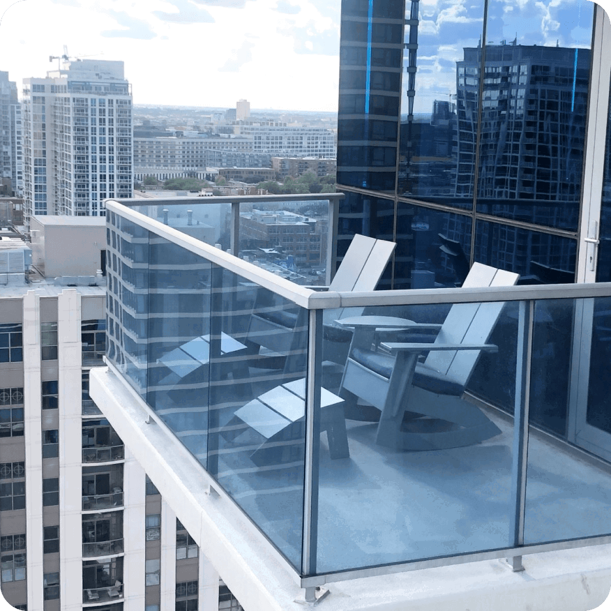 Emmet rocker chairs in white on a balcony with glass railing, overlooking a city skyline and tall buildings.