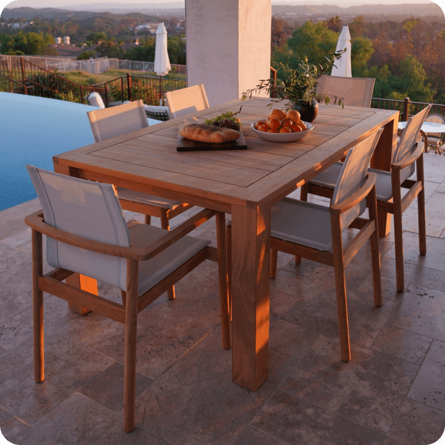 Capri table with wood top and matching chairs on a patio, styled with bread and fruit in warm sunset light.