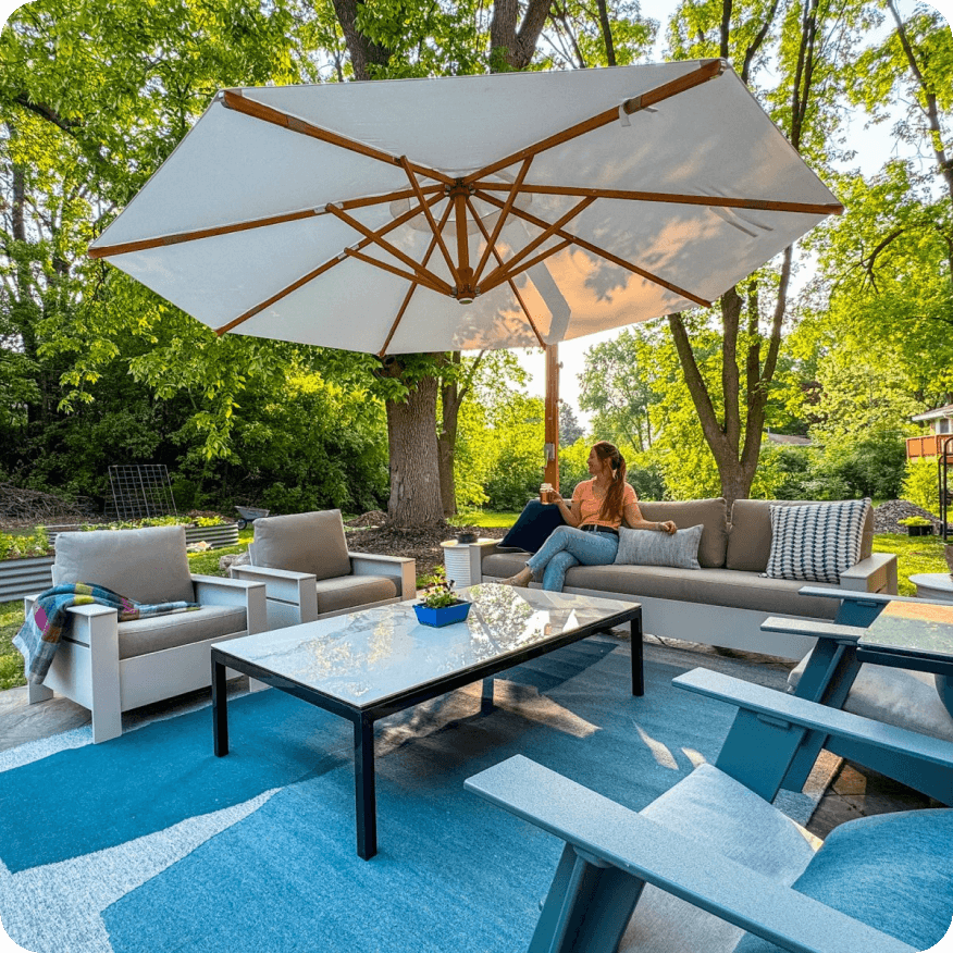 Rayo sofa with beige cushions and matching chairs under a large white umbrella, arranged around a glass top table.