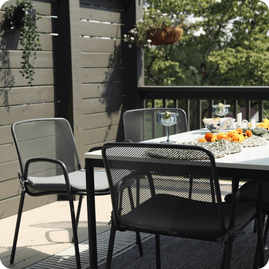 Aruba chairs in black mesh around a Parsons outdoor dining table, set with glassware on a deck with wood railing.
