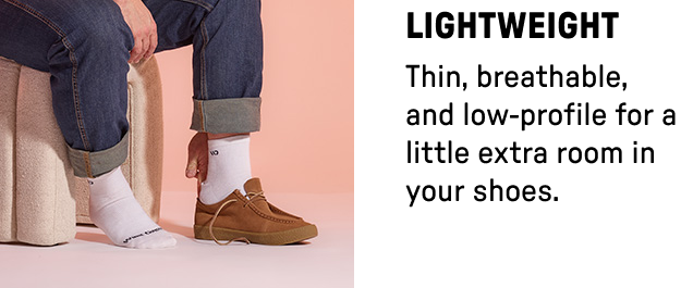 Man's legs wearing white lightweight crew socks with one shoe on showing low profile socks fit in shoes