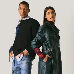 Man en vrouw staan rug aan rug, gekleed in moderne gelaagde outfits met denim, leren trenchcoat en casual schoenen op een neutrale achtergrond.