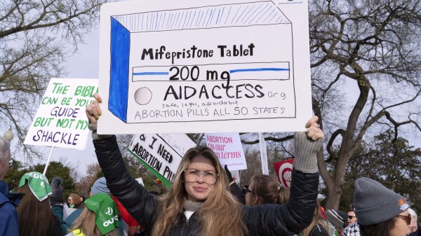 Abortion-rights activists protested outside the Supreme Court. One person holds a sign over her head that shows a drawn box of the mifepristone tablet. 
