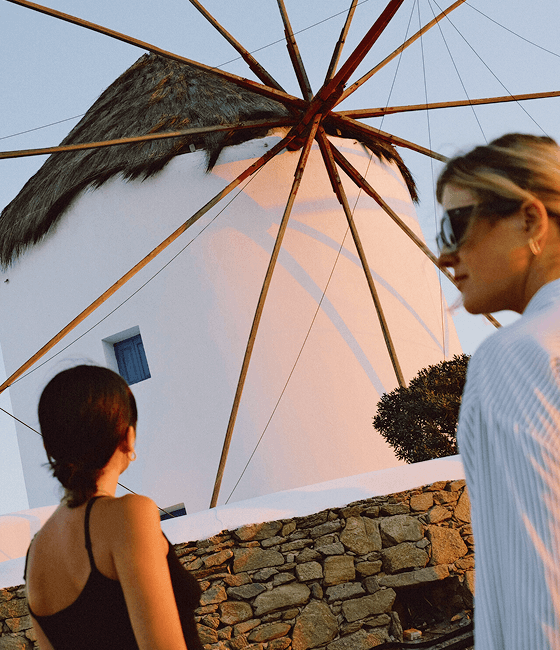 Two women sightseeing walk past a traditional white windmill.