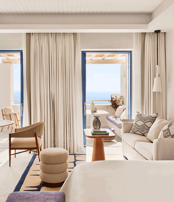 A neutral-toned hotel room with blue-trimmed doors opening to a sea-view balcony.