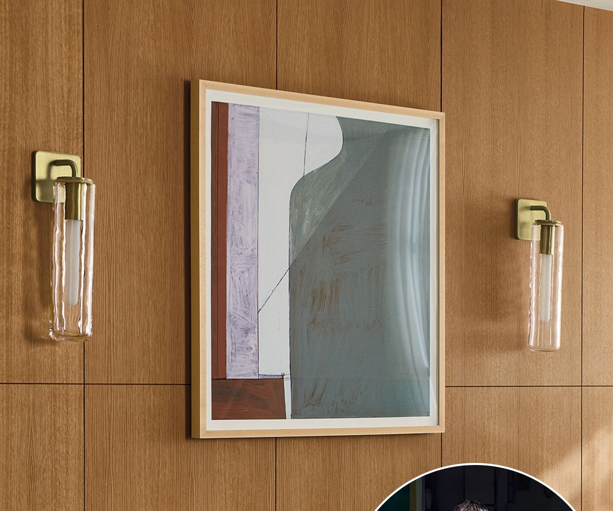 Framed abstract artwork with grey, white, and muted tones displayed on a wood paneled wall between sconces.