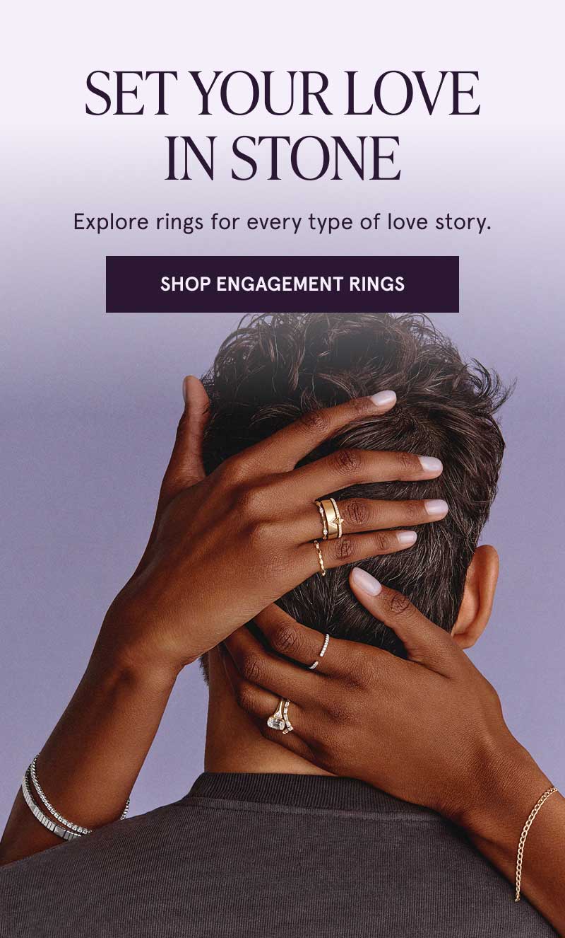 Female holding male’s head, focus on gold-set rings with diamond details. Explore rings for every type of love story. Click here to shop engagement rings