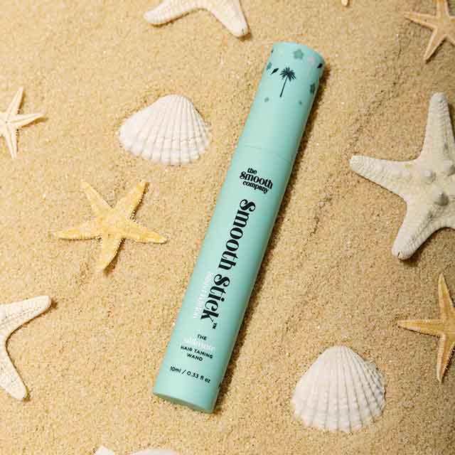A turquoise 'Smooth Stick' product lies on sand surrounded by starfish and seashells.