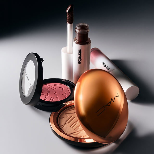 Assorted M.A.C makeup products including compact powders and lip gloss are arranged on a reflective surface.