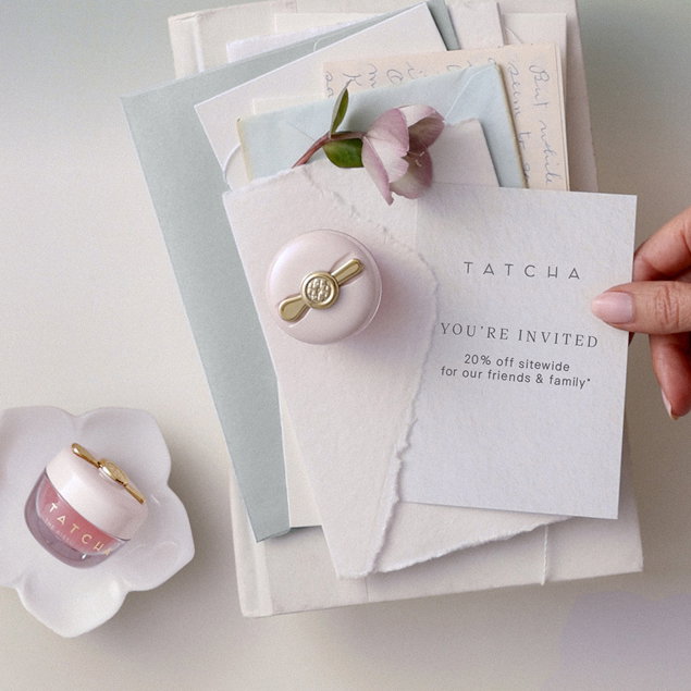 A selection of Tatcha lip products and an invitation and flower in an envelope