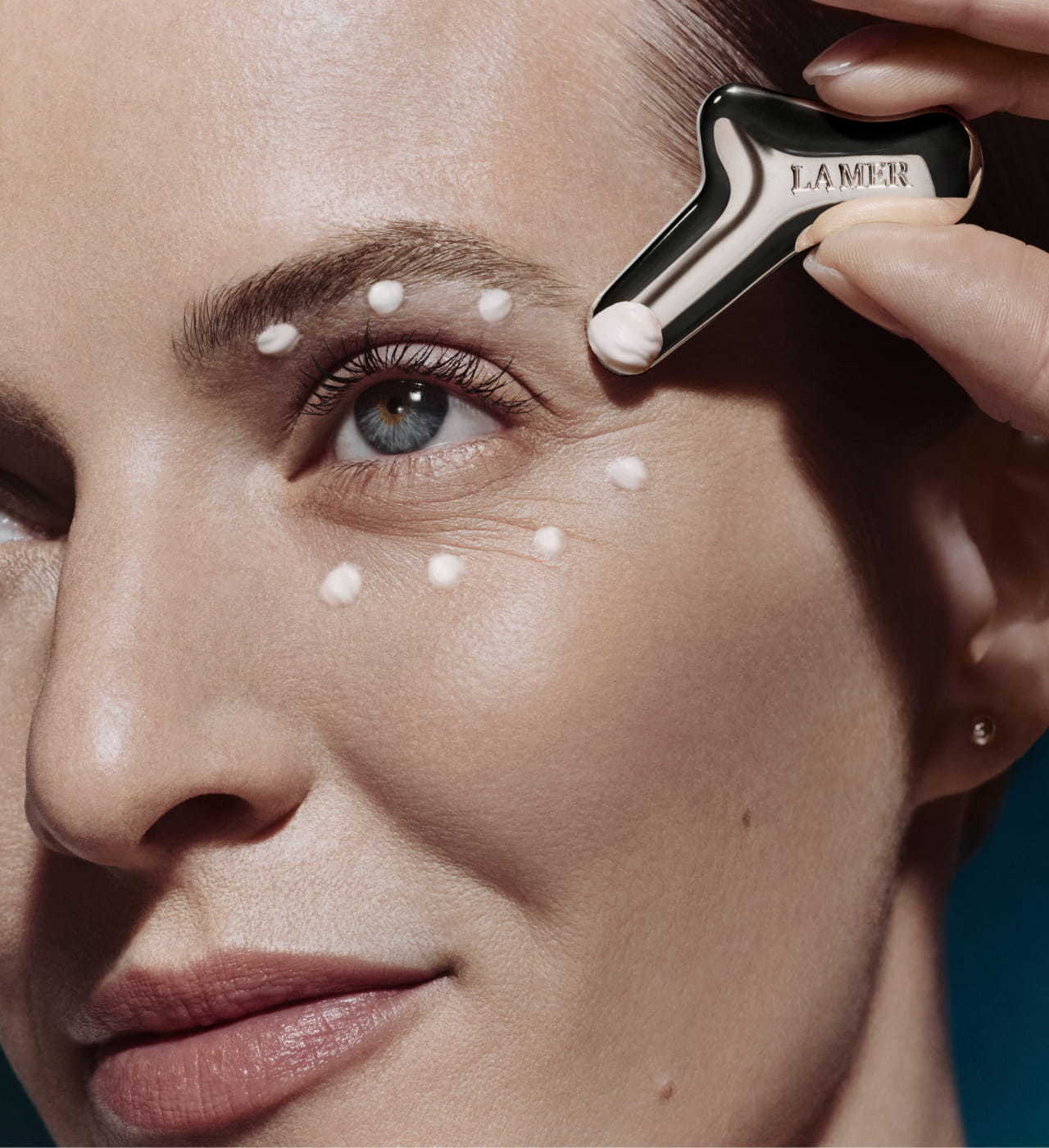 Close-up of woman face with hand applying The Rejuvenating Eye Cream.