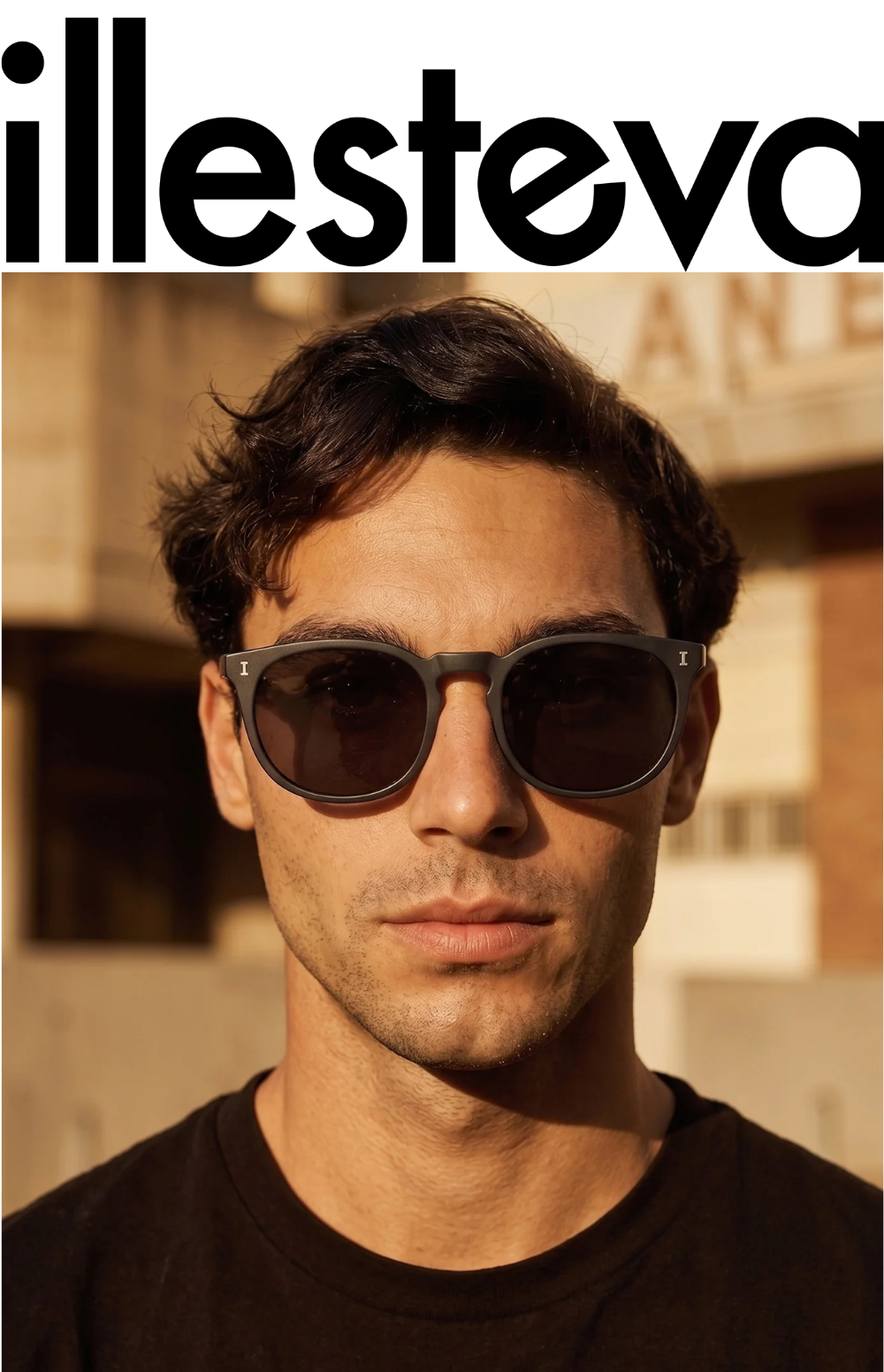 A close-up portrait of a man with dark, wavy hair wearing the Eldridge sunglasses in a matte black frame with dark lenses. The illesteva logo is visible in large black letters at the top.