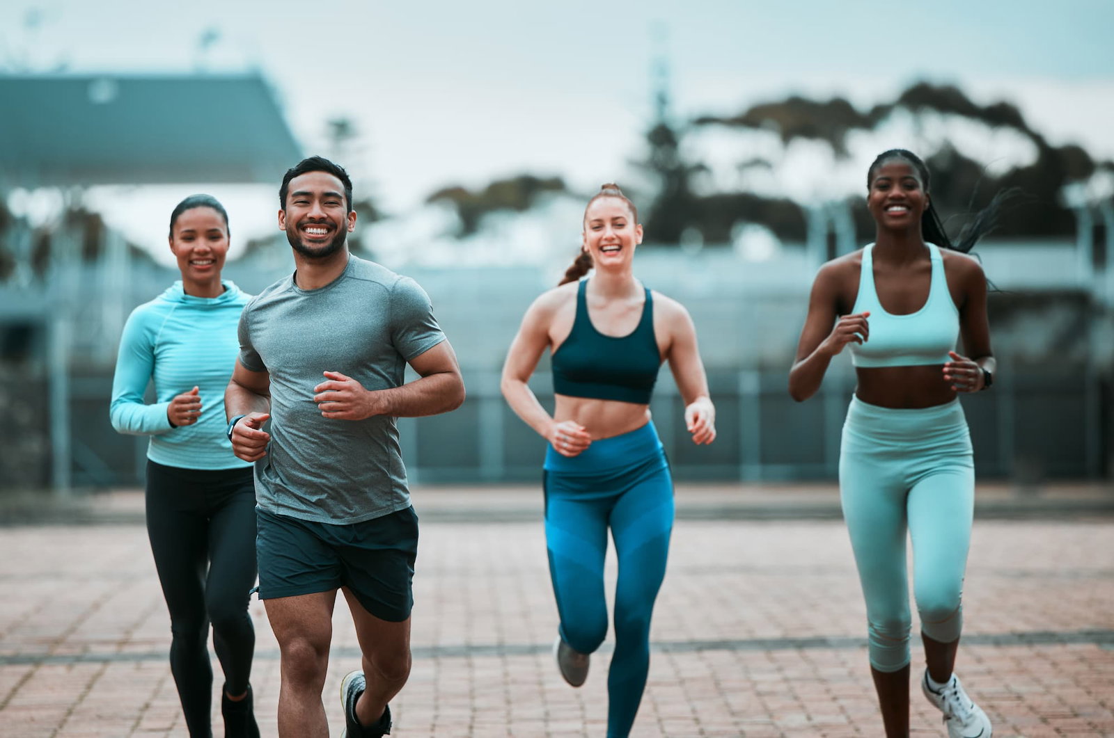 1 man and 3 women running outside on a road with pavers