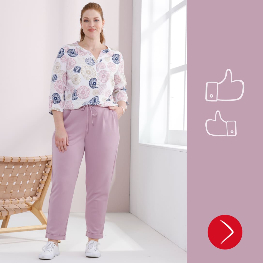 Een model draagt een witte blouse met patroon en lichte, losse broek met trekkoord. 