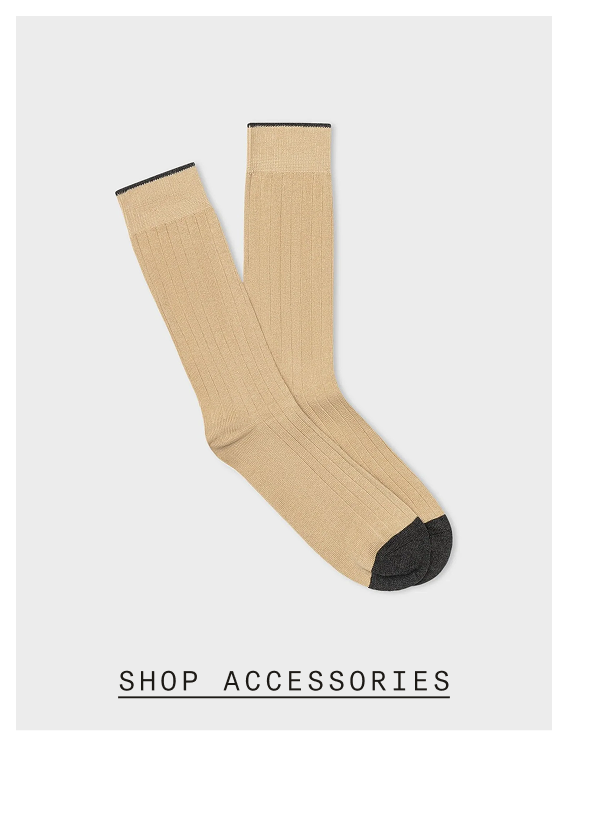 Pair of tan ribbed dress socks with black contrast toe and cuff, displayed flat against a light gray background. SHOP ACCESSORIES