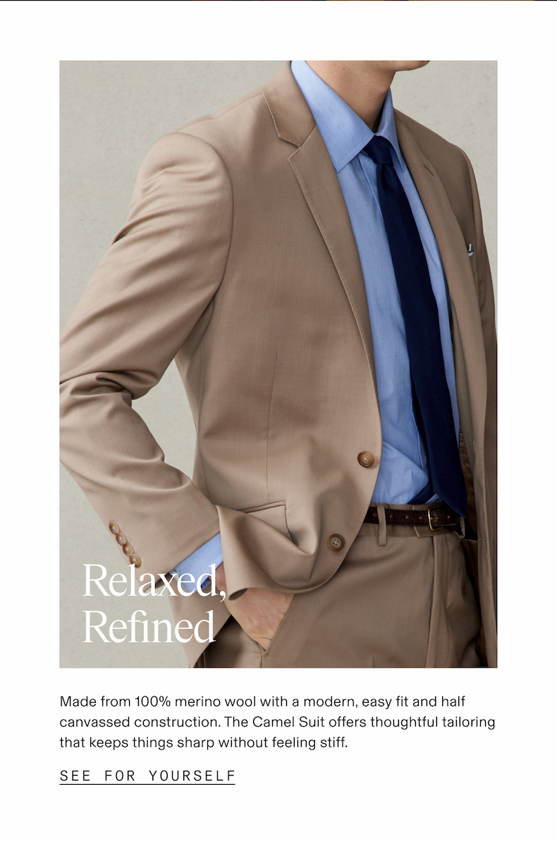 Close-up of a man from the chest down wearing a camel suit jacket, light blue dress shirt, navy tie, brown leather belt, and camel trousers, posed with hands in pockets against a neutral gray background. Overlaid text reads: Relaxed, Refined. Below the photo: Made from 100% merino wool with a modern, easy fit and half canvassed construction. The Camel Suit offers thoughtful tailoring that keeps things sharp without feeling stiff. SEE FOR YOURSELF