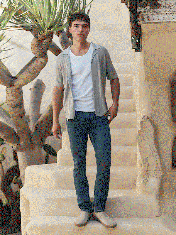 Animated image of a man wearing blue denim jeans paired with a white tank and light grey knit short sleeve button up top.