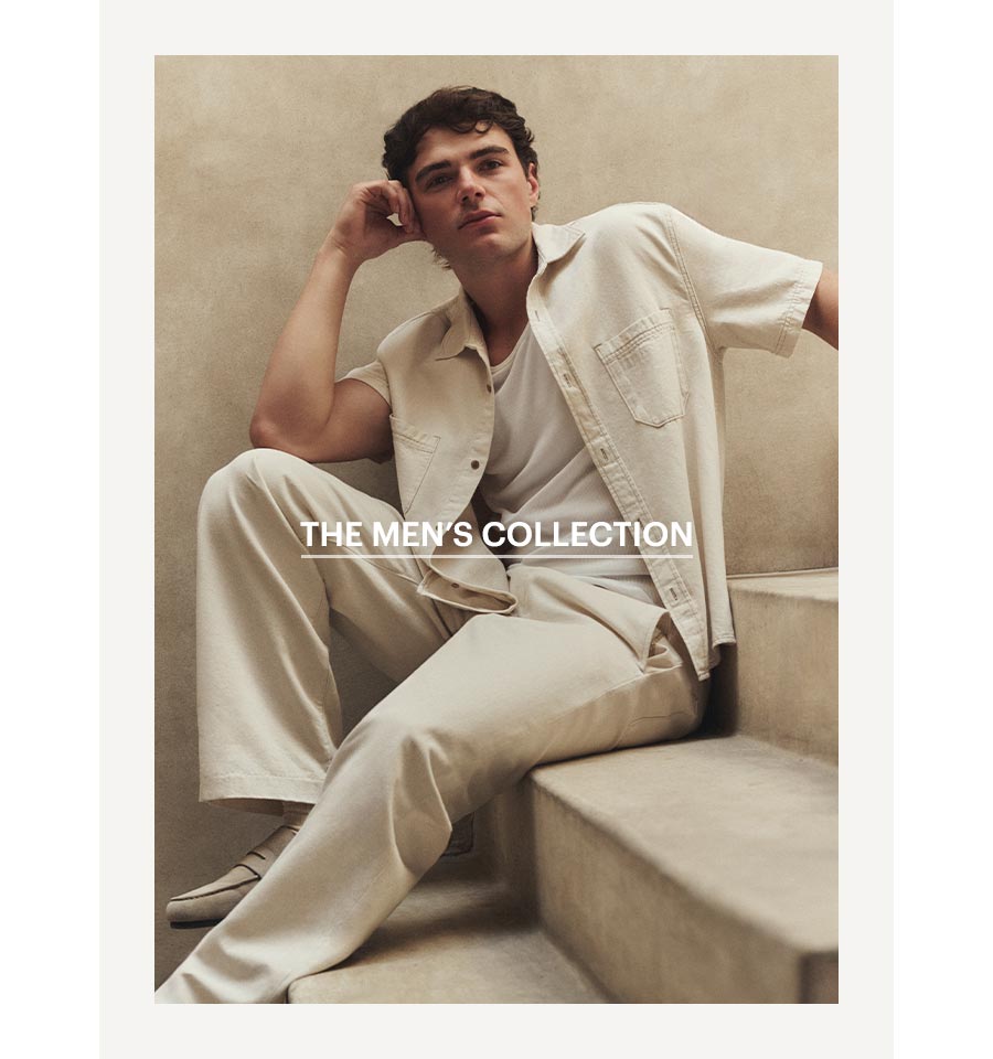 A man sitting wearing an ecru colored denim short sleeve shirt, white tank top and ecru colored wide leg tie-waist pants.  Shop The Men's Summer '26 Colletion.