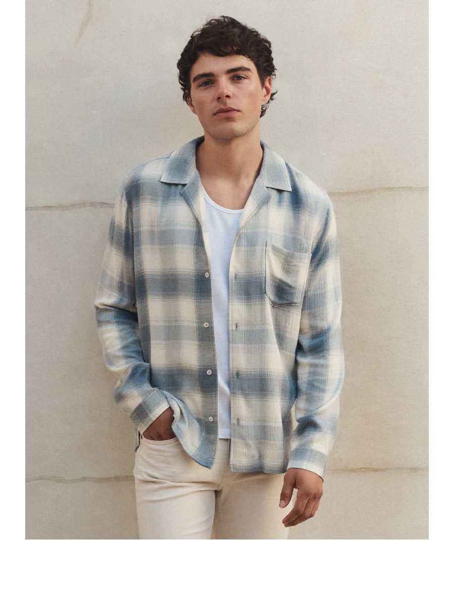 A man wearing a light blue and ivory plaid flannel shirt and cream colored denim jeans.