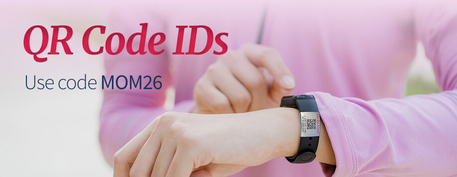 Close-up of a wrist wearing a black sports band with a silver MedicAlert metal tag. The tag features the MedicAlert logo and a QR code. A second hand is visible pointing towards the QR code. Red title text reads 'QR Code IDs'. Below the title, smaller text says, 'Use code MOM26'.