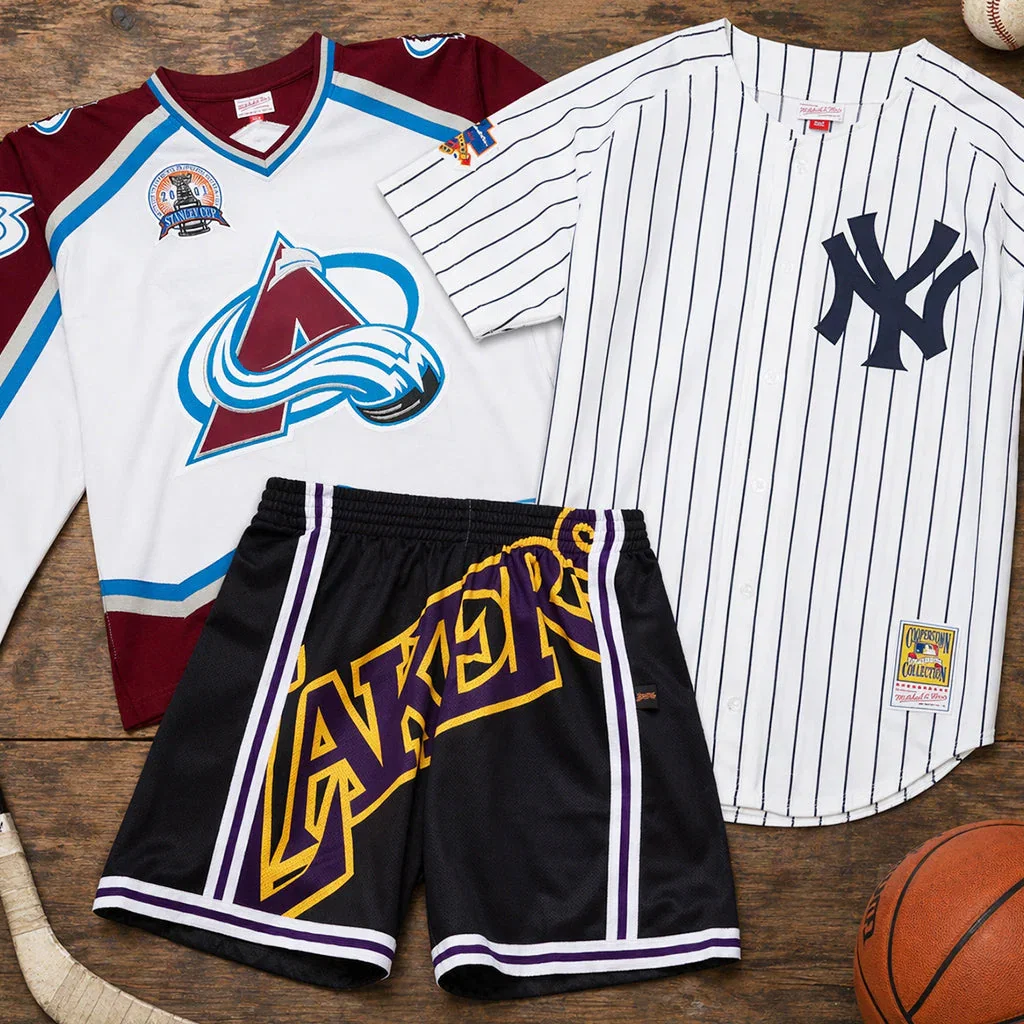 Mitchell & Ness vintage sports jerseys and shorts displayed on wood background with baseball and basketball.