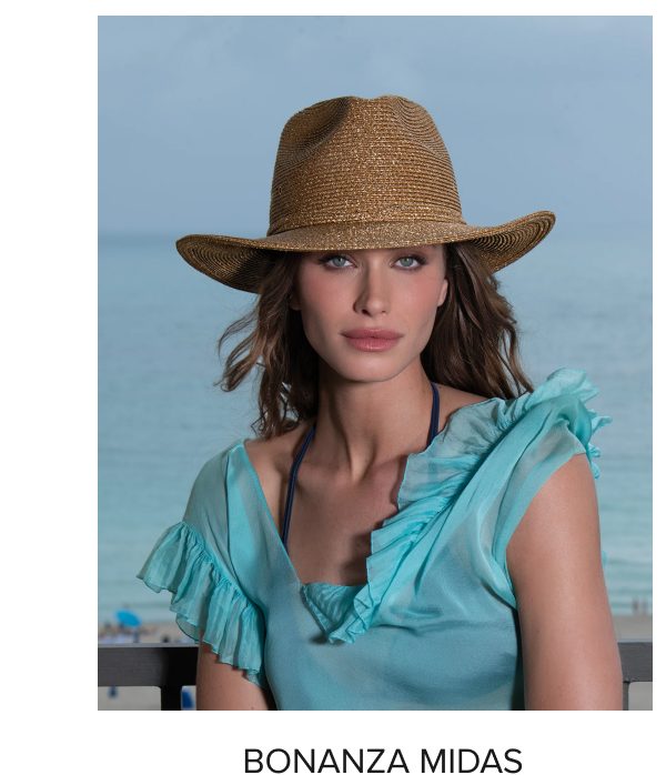 A woman wearing a straw hat and a light blue ruffled top, with the ocean in the background.
