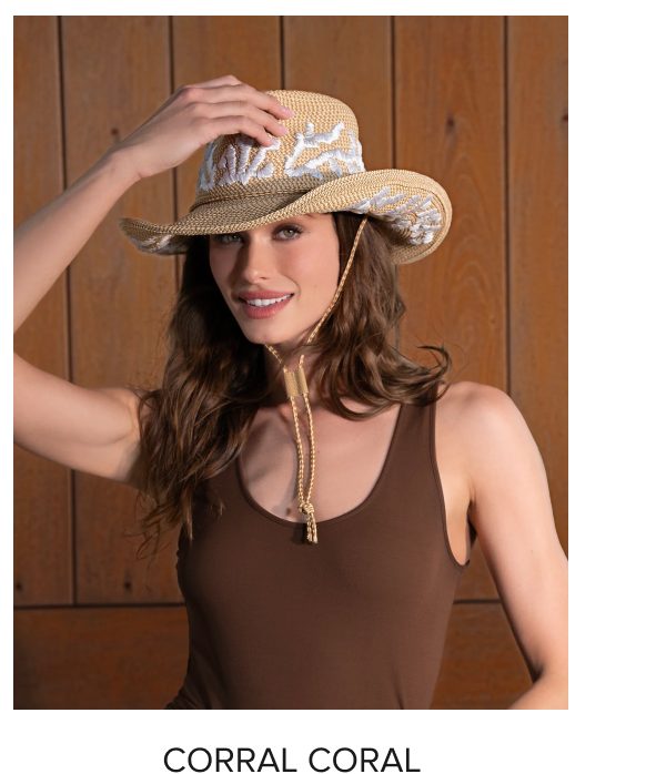 A woman wearing a straw hat with a floral design, smiling and touching the brim.