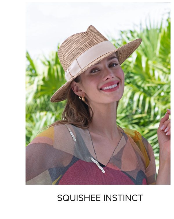 A smiling woman wearing a straw hat and a colorful top, surrounded by greenery.